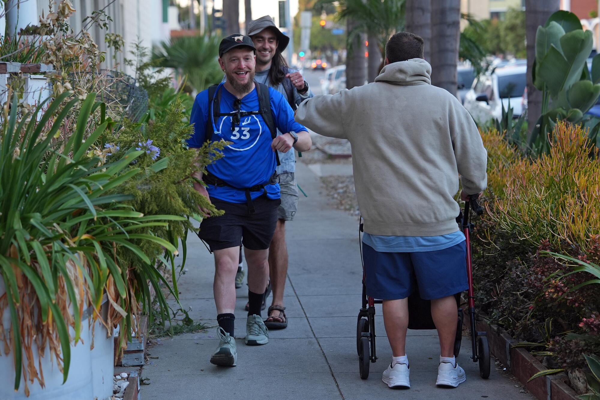 A man using a walker fist bumps two men walking by him.