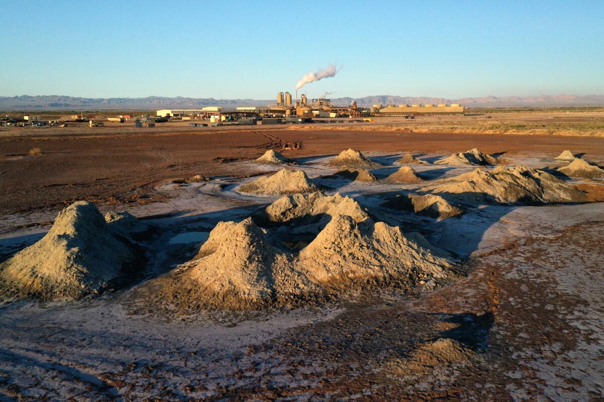 Mounds of dirt and areas of bubbling hot water bubble near an industrial facility.