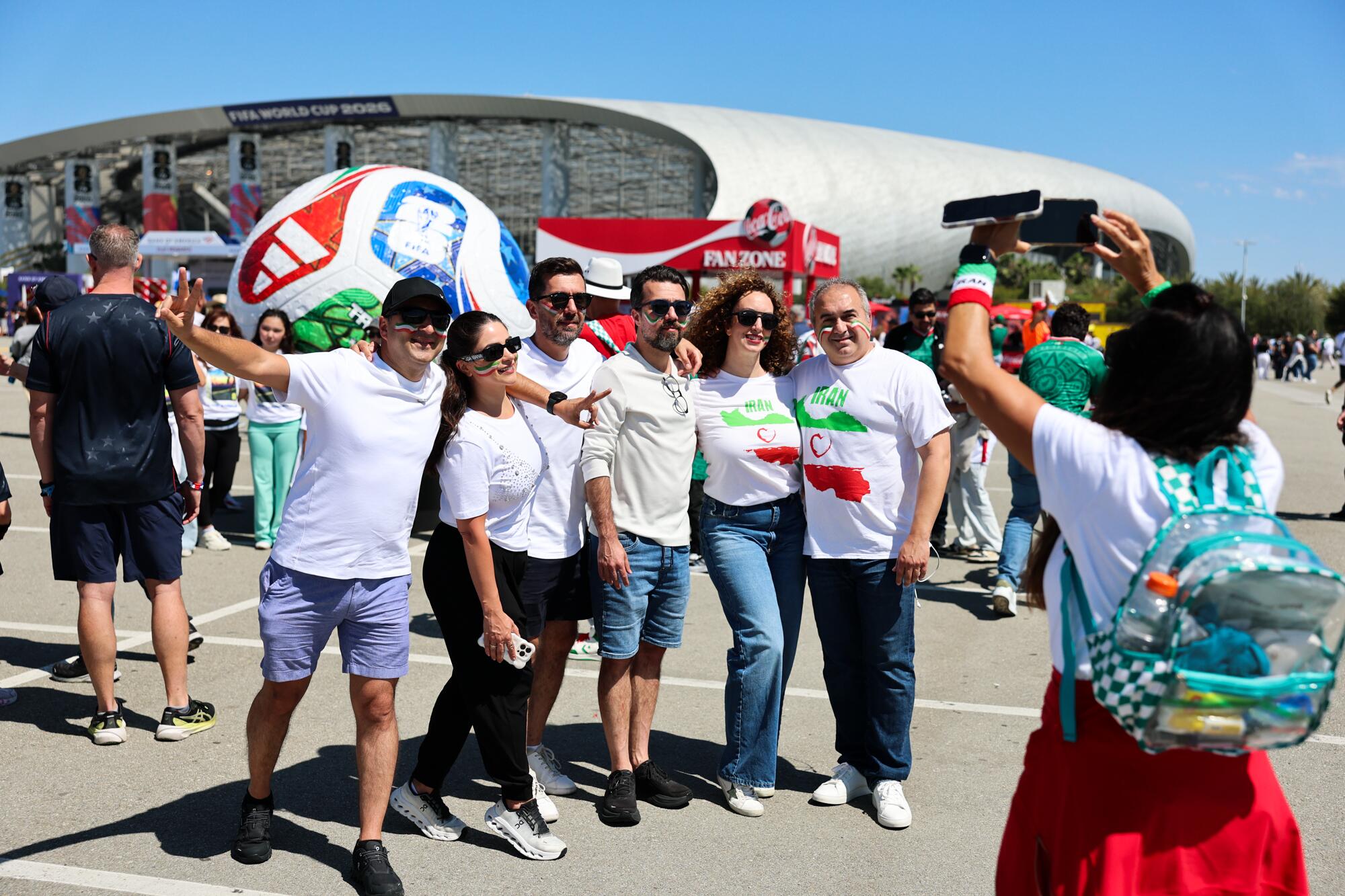 A group of six men and women in white T-shirts pose for a photo in a parking lot.