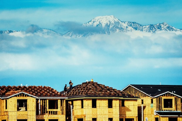A sea of low hanging clouds surrounds the snow-capped San Gabriel Mountains as roofers stack roof tiles onto new homes under construction in Chino on Thursday, Dec. 5, 2019. (Photo by Watchara Phomicinda, The Press-Enterprise/SCNG)
