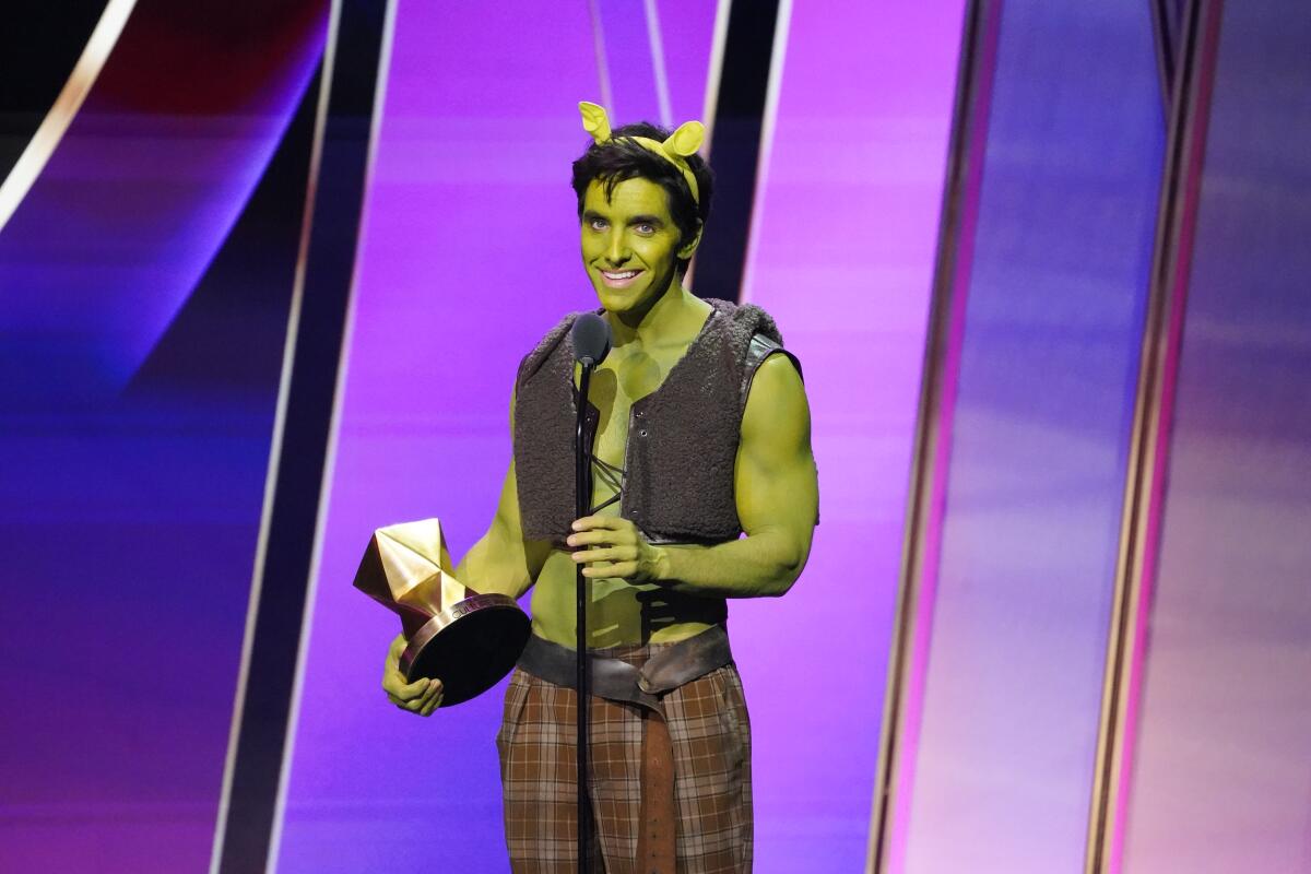 A man whose skin is painted green appears on a stage holding an award
