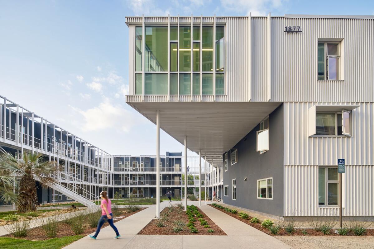 A horizontal view shows a three-story dorm building, with geometric elements, in which each unit faces an open-air walkway.