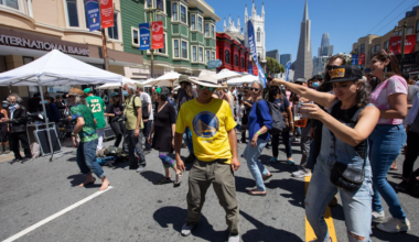 a man shows off his moves in the street during a festival, with the Transamerica pyramid behind him