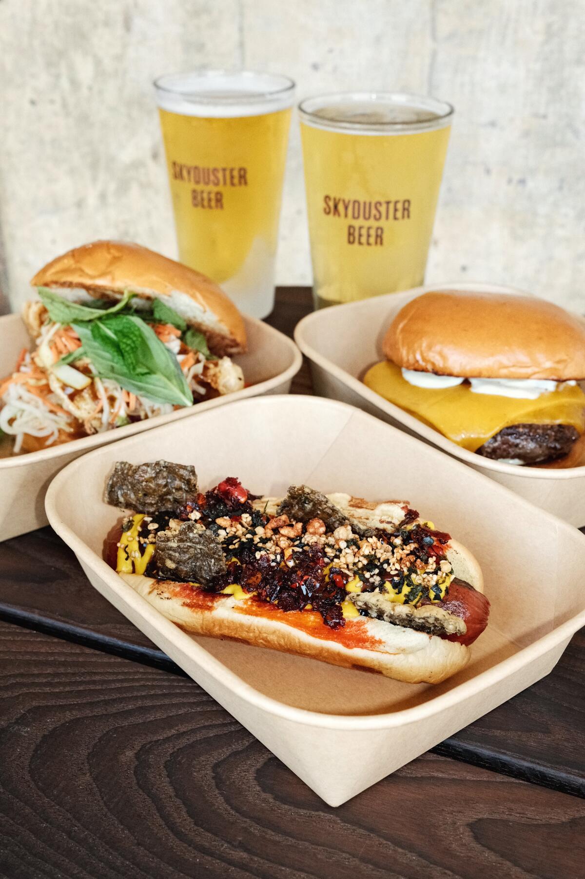A furikake- and chili crisp-topped hot dog, masa-dredged Thai fried chicken sandwich, and cheeseburger on a wood table