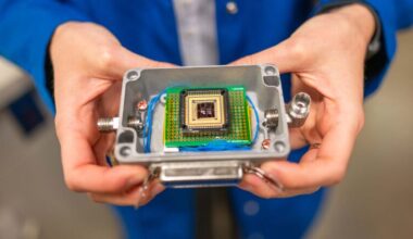 A pair of hands holds a small plastic box that contains a complex electronic chip.