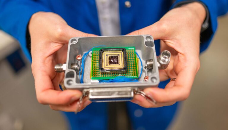 A pair of hands holds a small plastic box that contains a complex electronic chip.