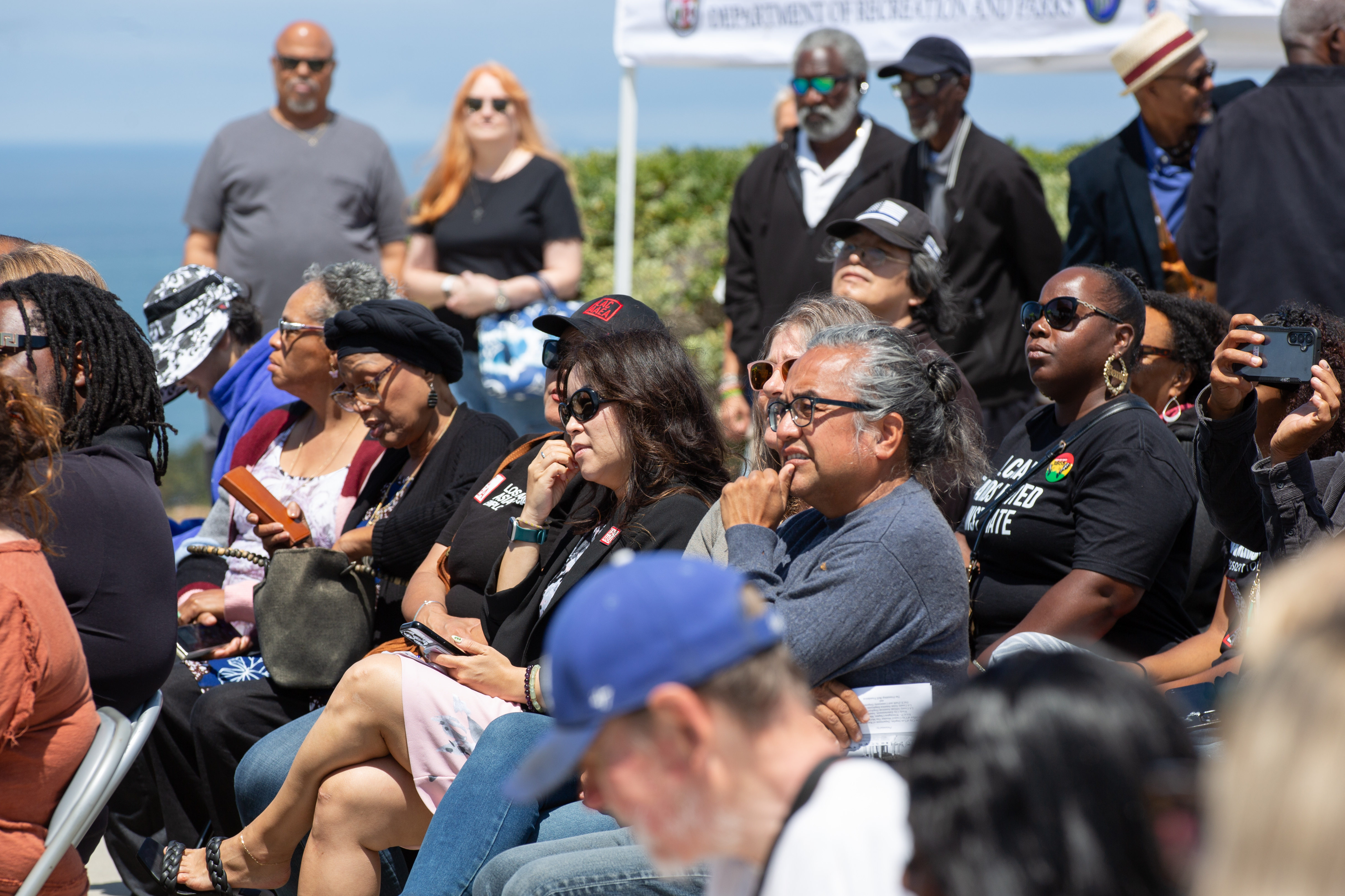 Dozens of attendees listen to speakers and singers during a...