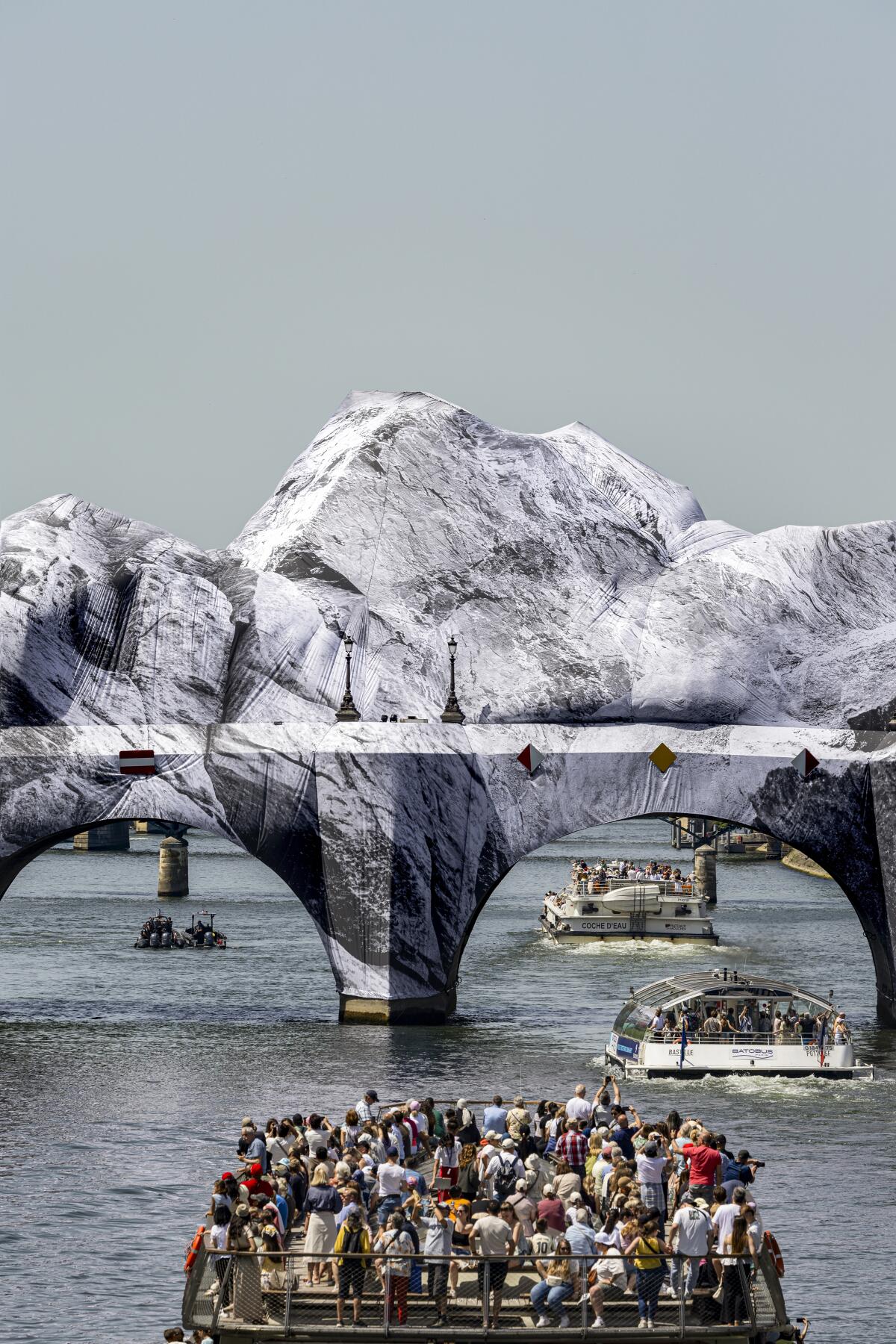 Passengers on a boat look at a mountain over a bridge.
