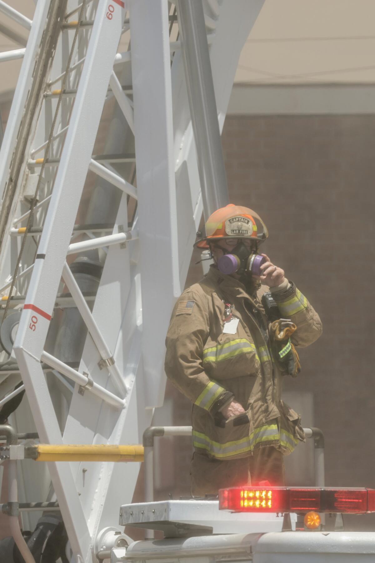 A Los Angeles Fire Department captain wears a respirator while leaning against a fire truck ladder.