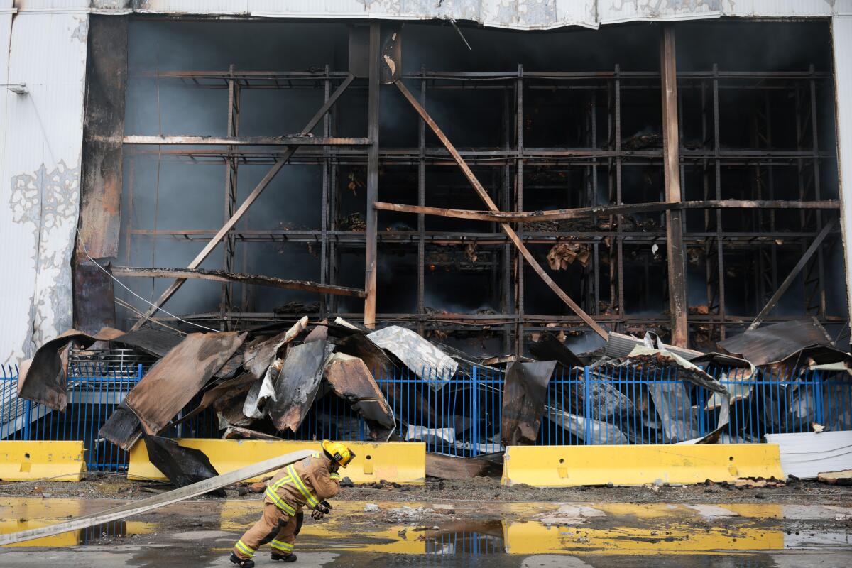 A Los Angeles Fire Department firefighters drags a water hose alongside the Lineage cold storage facility.