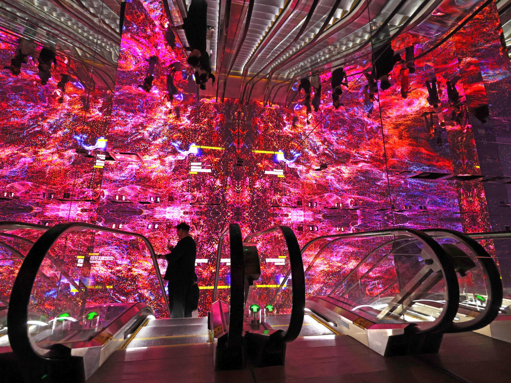 A visitor takes the escalator surrounded by pink lighted screens