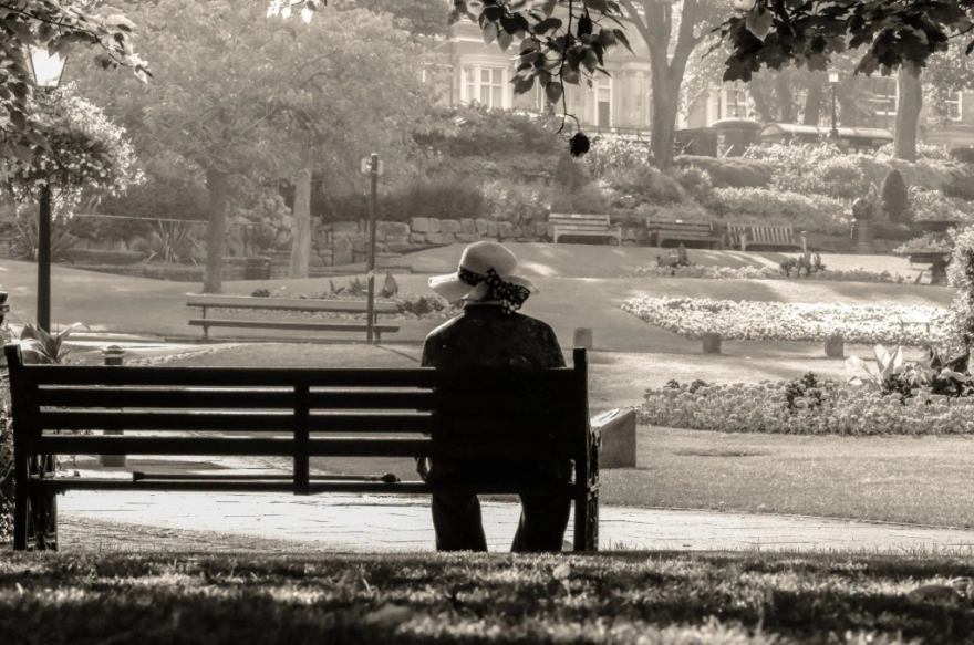 An aging woman sits alone on a park bench in this photo illustration.
