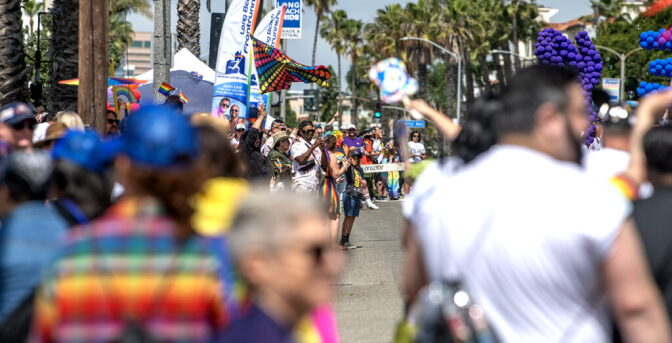 A crowd of people celebrate along a street wearing colorful shirts and holding flags.