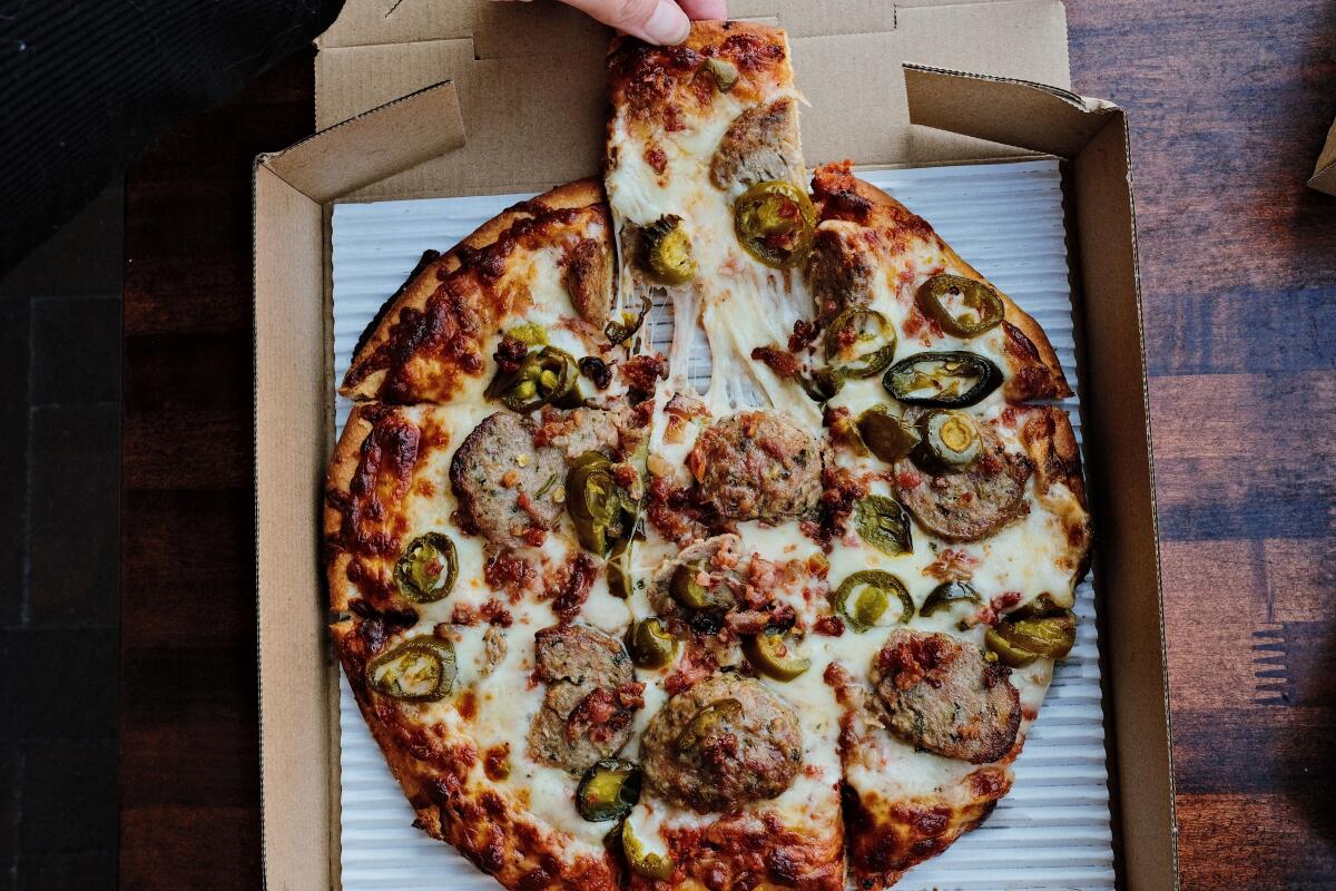 A hand pulls a square slice of meatball-and-jalapeño-topped tavern style pizza at Rance's Chicago Pizza in Long Beach
