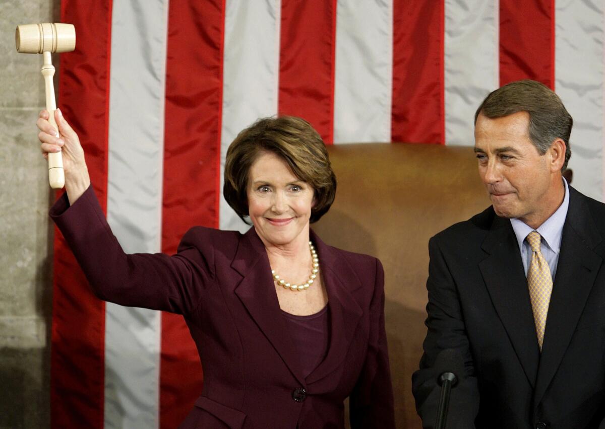 Nancy Pelosi smiles and holds up the speaker's gavel as John Boehner smiles.