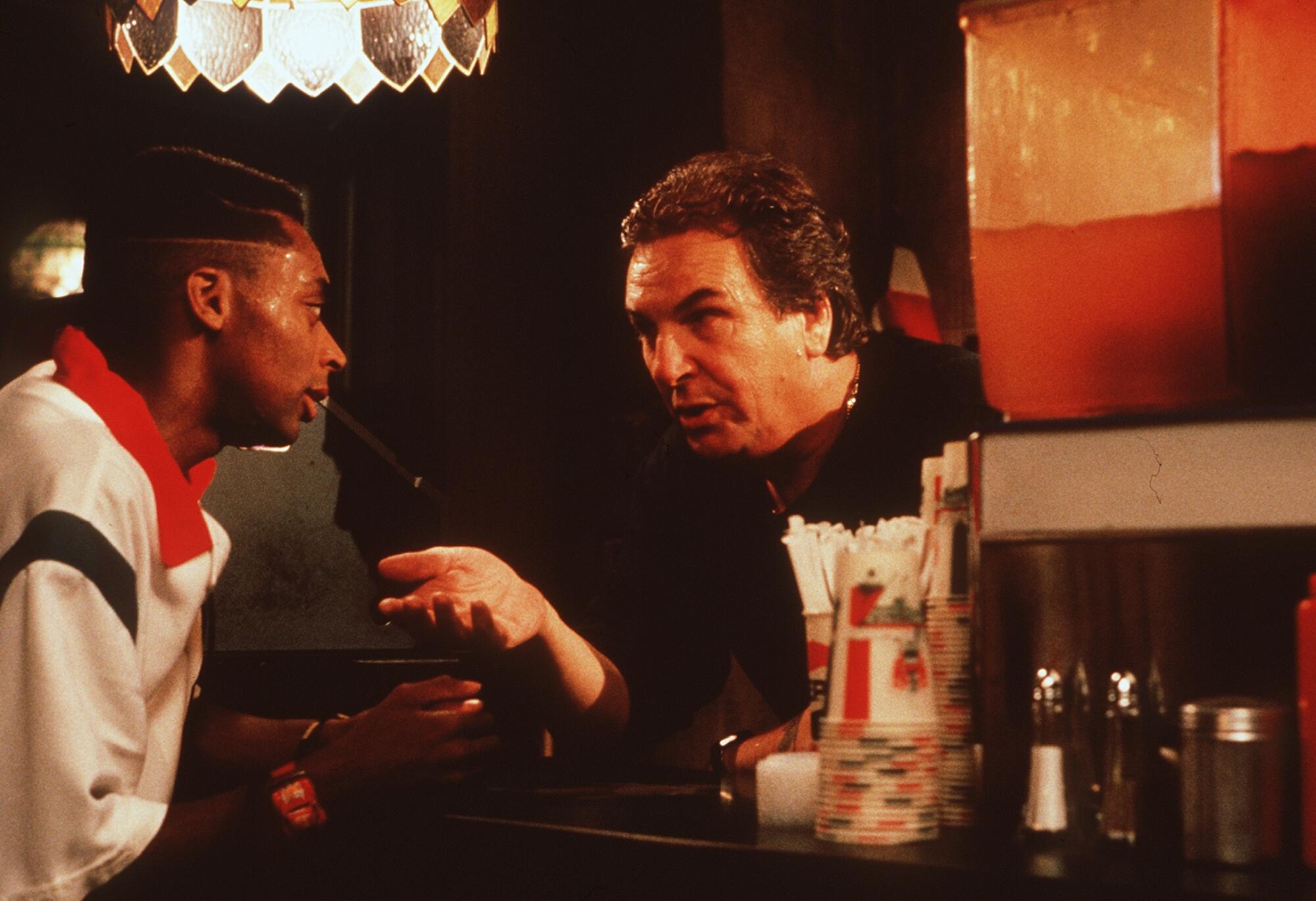 A delivery driver and a pizzeria owner argue across a countertop.