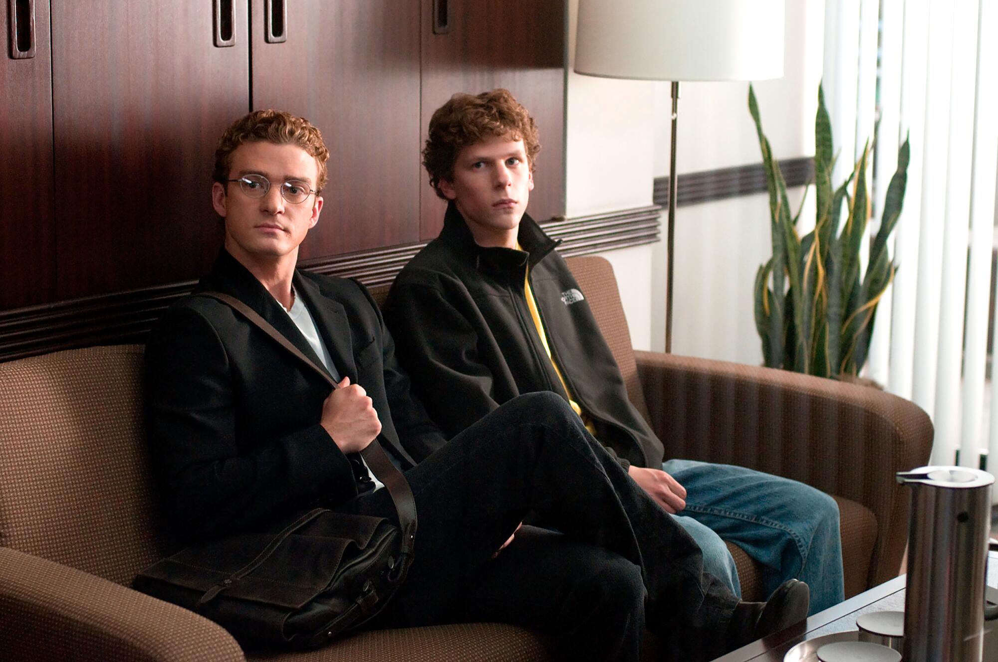 Two young men sit uncomfortably on a couch, waiting for an appointment.