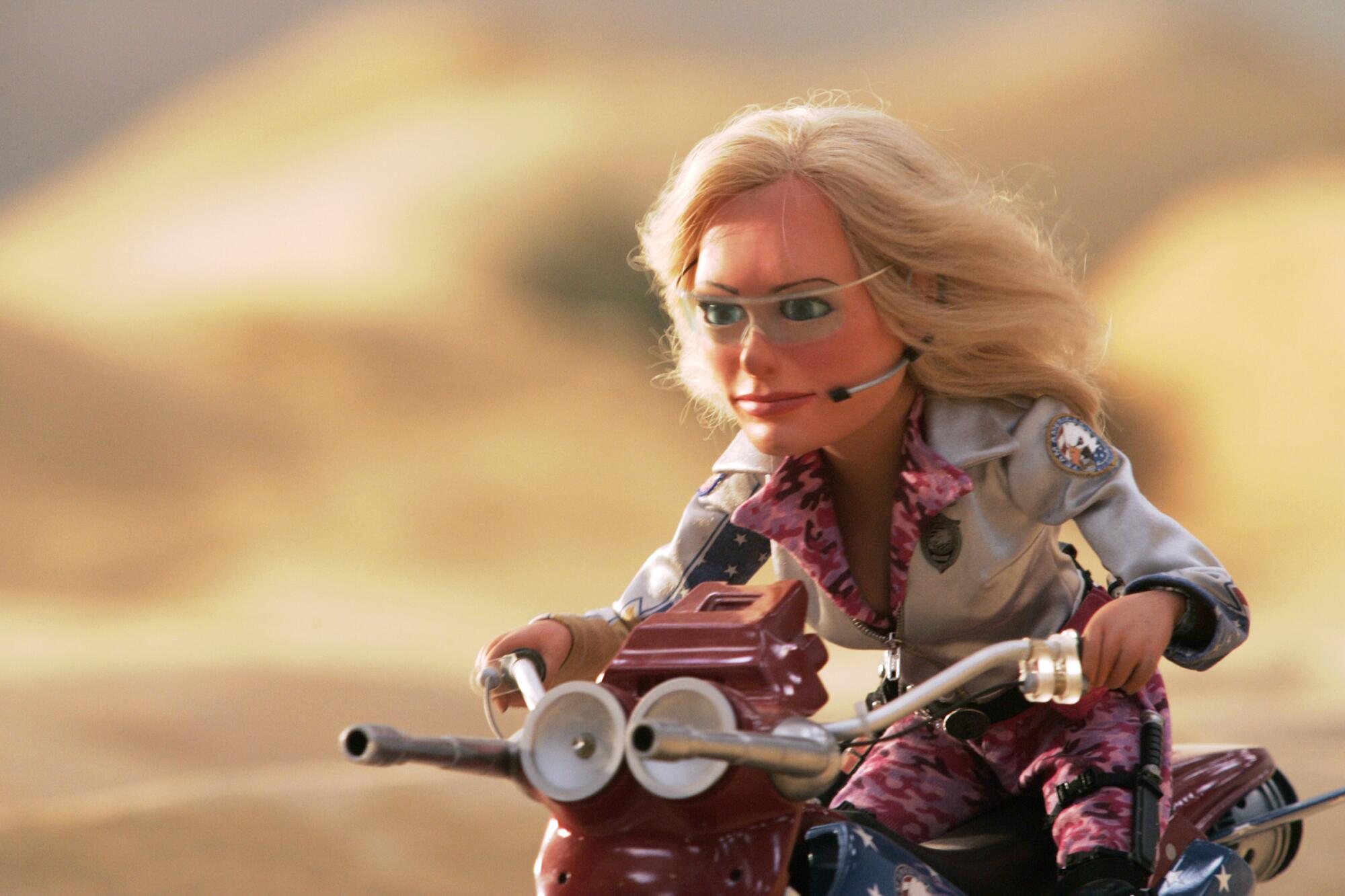 A woman puppet on a motorcycle races into action.