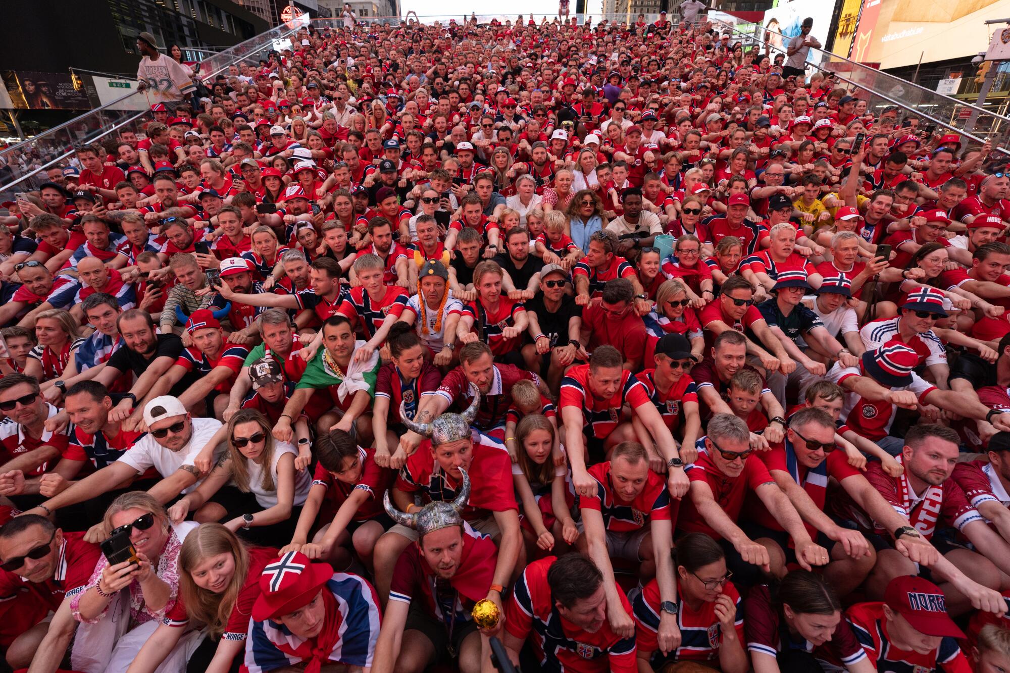 A group of people sits closely together and mimic rowing, with the majority wearing red shirts