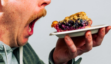 A man with a mustache holds a plate with a slice of berry crumble pie close to his face, looking at it intently.