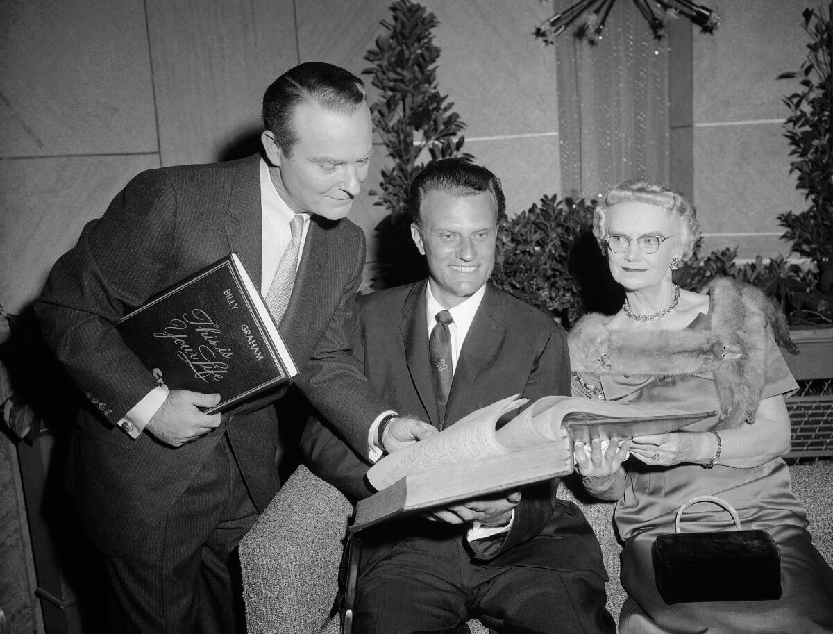 Ralph Edwards thumbs the pages of a Bible held by evangelist Billy Graham.