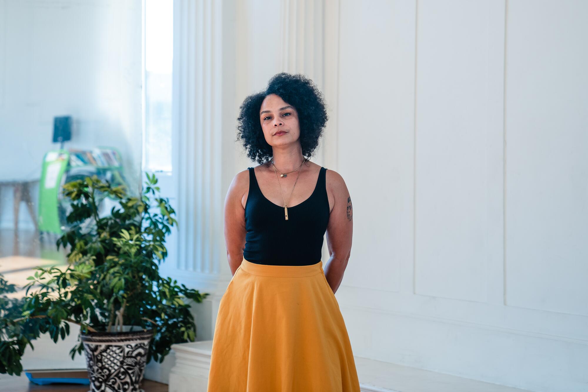 Rosalie Tucker stands near a house plant in a studio. 