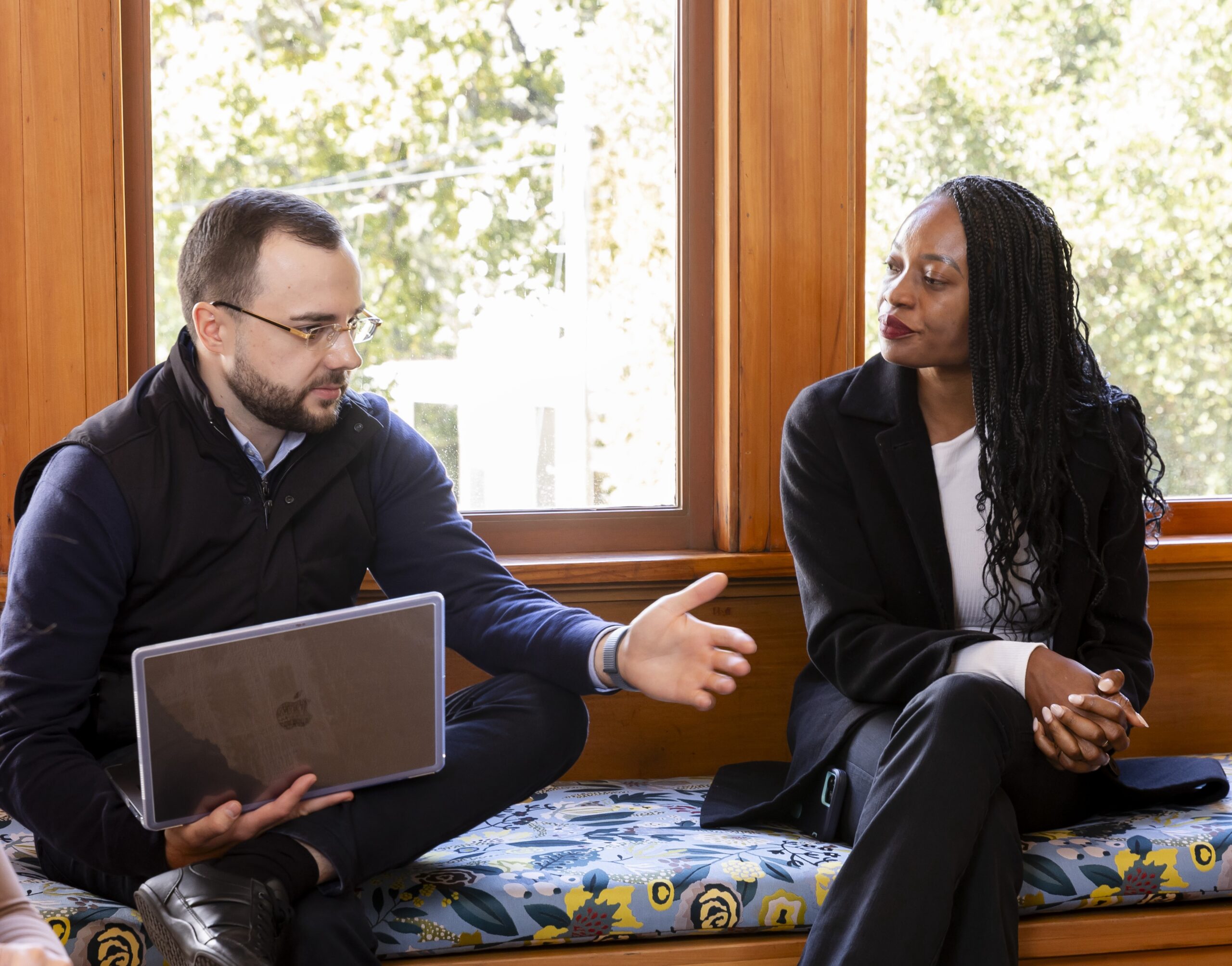 Man with laptop in his lap talking to a woman