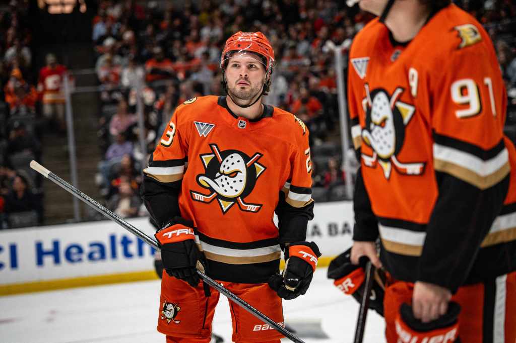 Two hockey players on the ice wearing orange jerseys with the number 3 on one and 91 on the other.