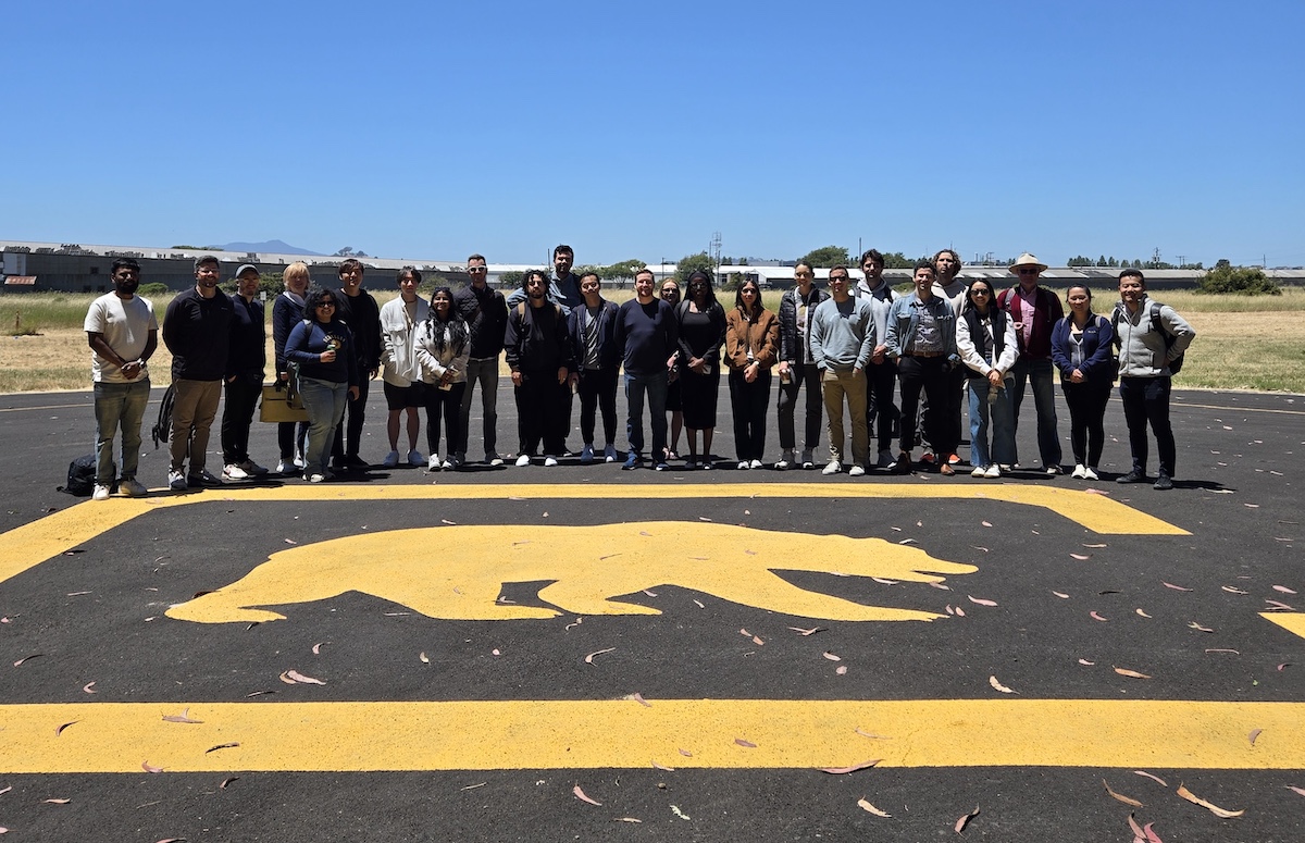 a group at the Richmond Field Station standing in front of a yellow cal bear painted  on the ground