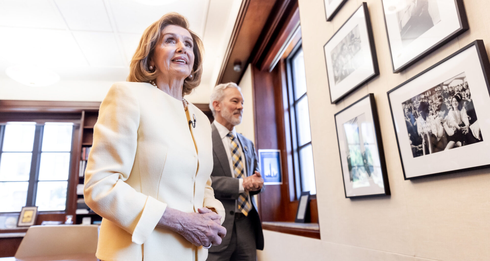 Nancy Pelosi, standing next to UC Berkeley Chancellor Rich Lyons, looking at photos on the wall.