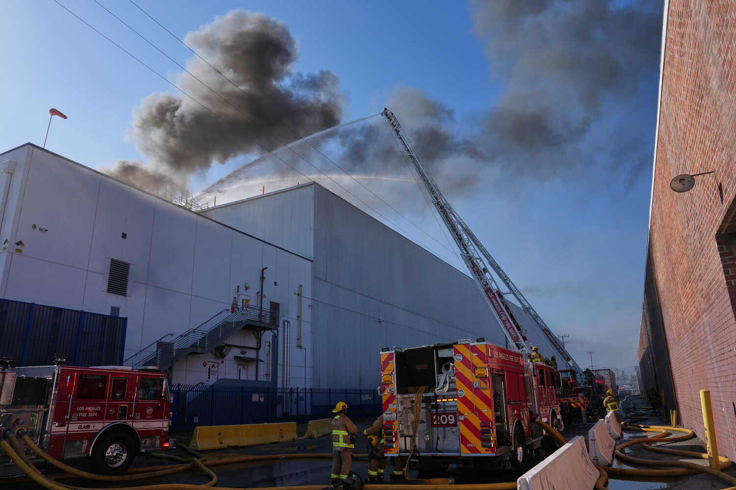 Fire trucks spraying water over a building with smoke billowing overhead.