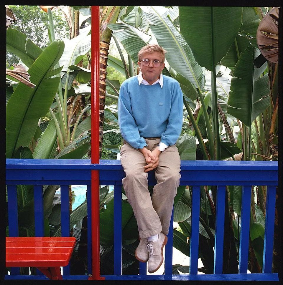 Portrait of English artist David Hockney, dressed in a light blue sweatshirt and khaki trousers as he sits on a dark blue railing, Los Angeles, California, 1987. (Photo by Anthony Barboza/Getty Images)