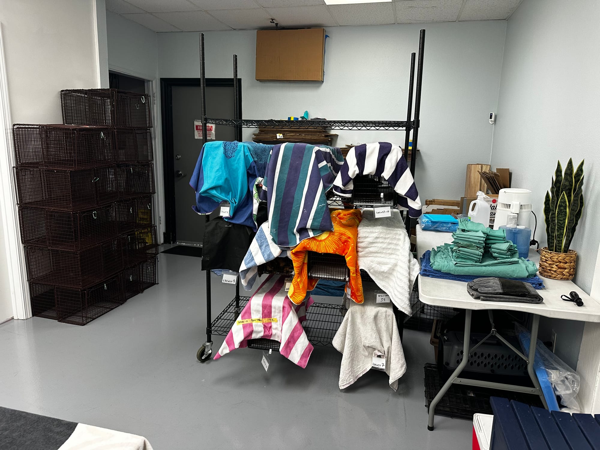 A room contain stacks of black pet cages and another shelf with about nine similar cages covered in colorful towels.