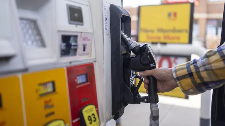 A hand in a plaid shirt holding a fuel nozzle refueling a car at a gas station pump