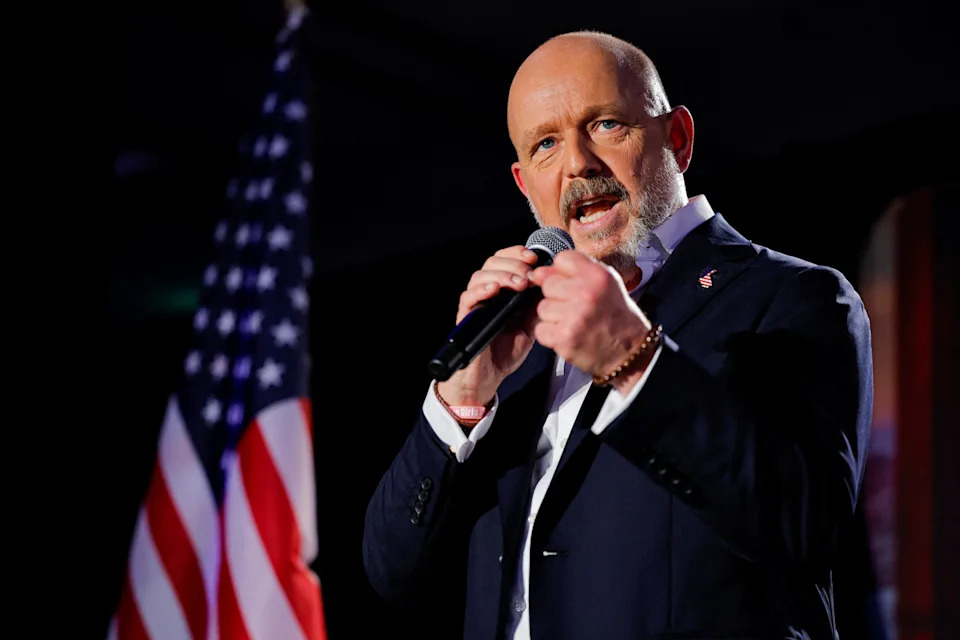 California Republican gubernatorial candidate Steve Hilton speaking into a microphone, with an American flag in the background.