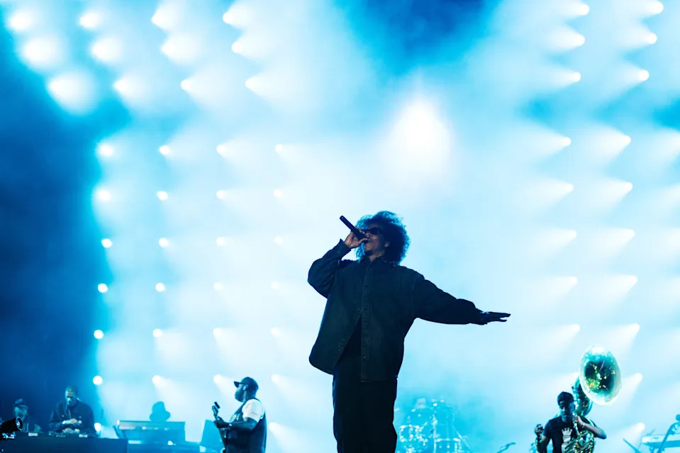 Jay-z on stage with bright blue lights in the background, musicians playing instruments on the side. This was at Roots Picnic 2026
