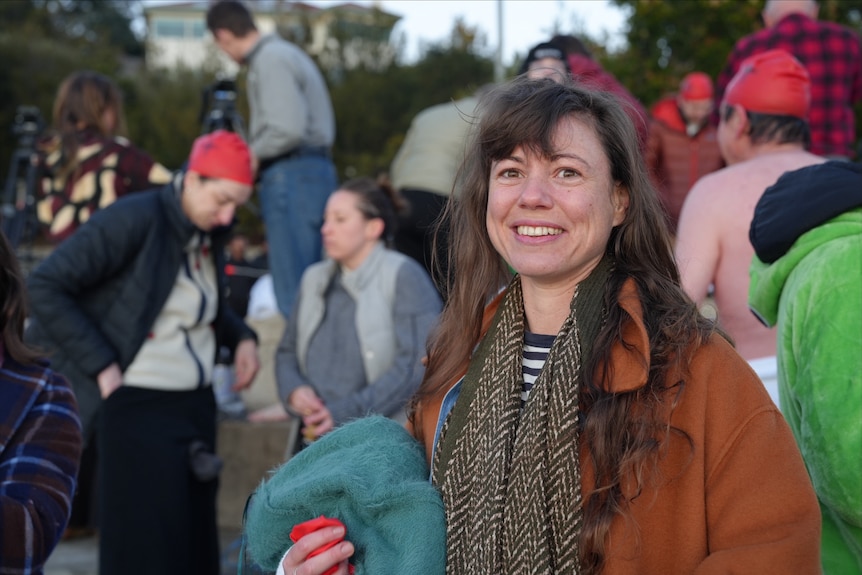 Jessica Nuel, a woman with brown hair and wearing a coat and scarf, smiles at the camera.