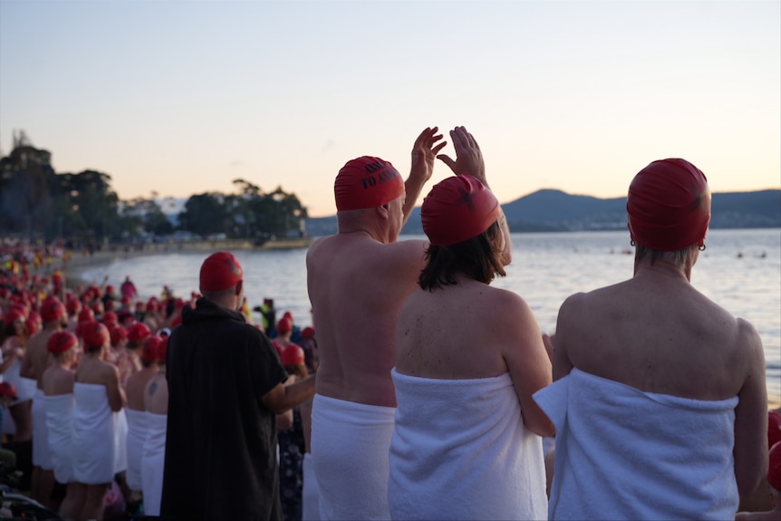 Groups of swimmers wearing towels prepare to enter the water for Dark Mofo's 2026 Nude Solstice Swim