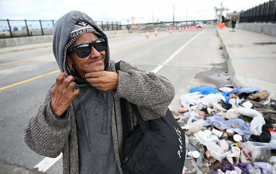 A homeless woman fixes her earring as she passes a pile of refuse along G Street Friday, Dec 26, 2025 in downtown Fresno.