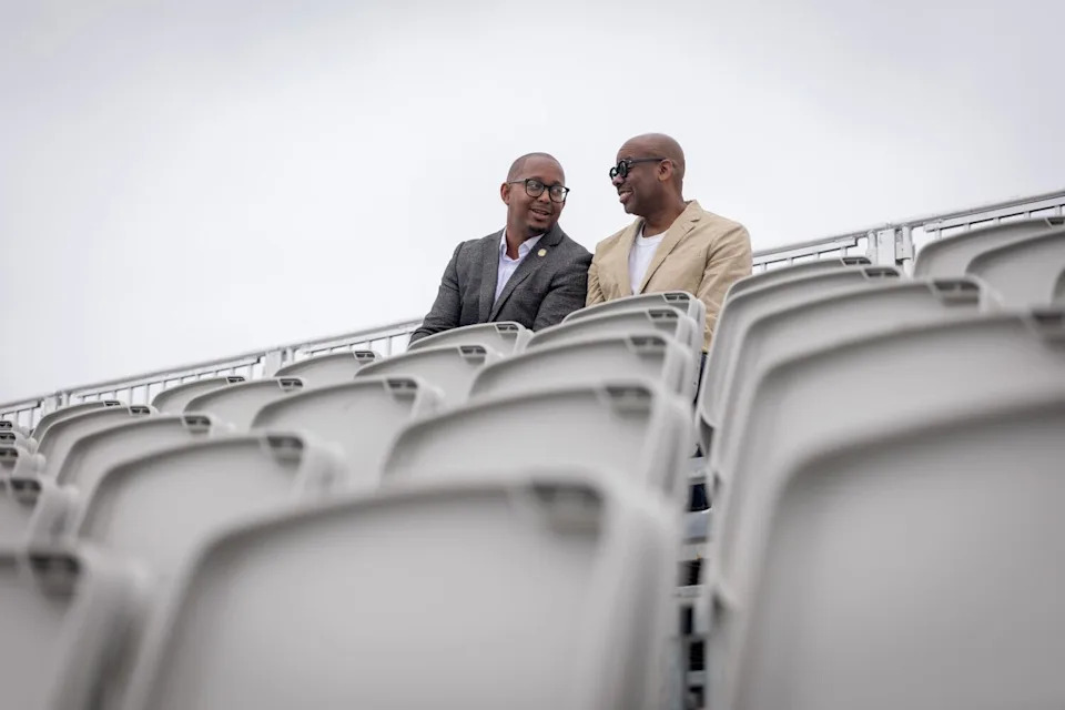 Two men sit on the top row of an amphitheater, chatting.