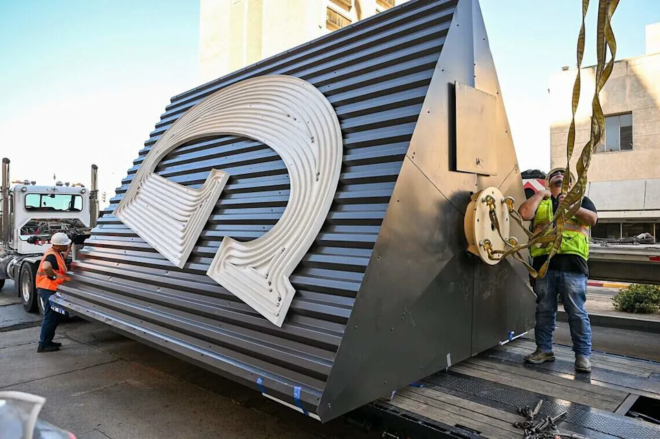 Workers attach the new Guarantee Savings G sign to a crane to be lifted to the top of the State Center Community College District building in downtown Fresno on Saturday, June 6, 2026. The new sign replaces the old one which was beyond repair.