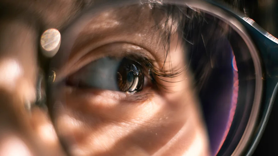 A close up of a person's brown eye behind the lens of the glasses.