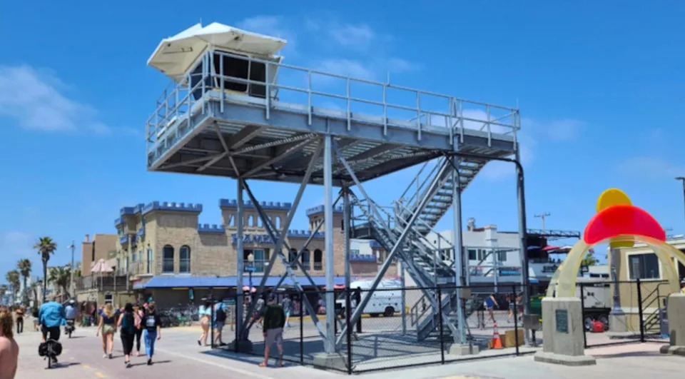 The structure features a traditional white lifeguard pod perched on top of a massive, multi-story web of steel scaffolding. Inside San Diego