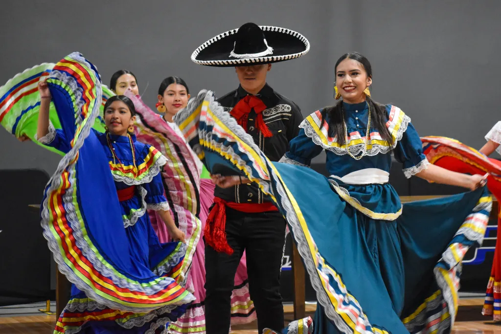 Dancers in vibrant traditional costumes perform a lively cultural dance with flowing skirts and colorful accessories.