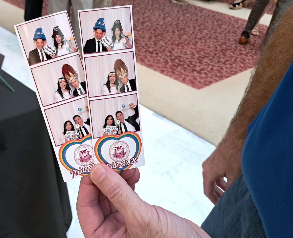 A hand holds a photo strip from Pride 2020 featuring multiple smiling individuals in whimsical costumes and props.