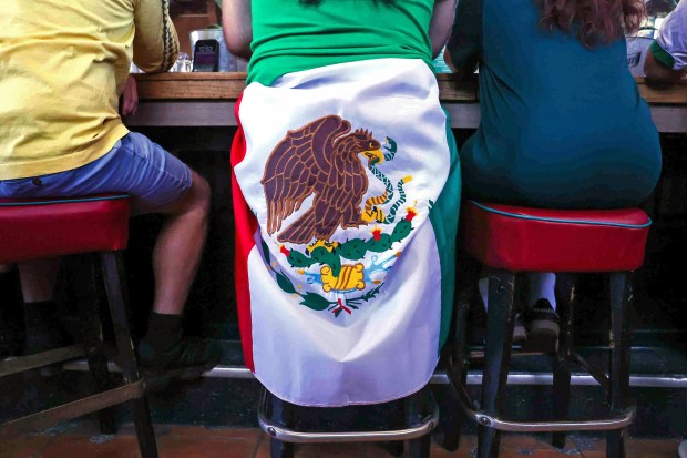 A Mexican fan wraps a flag around his waist as he and other soccer fans watch a live broadcast of the World Cup inaugural match between Mexico and South Africa at the Aloha Club in the Fruitvale district of Oakland, Calif., on Thursday, June 11, 2026. (Ray Chavez/Bay Area News Group)