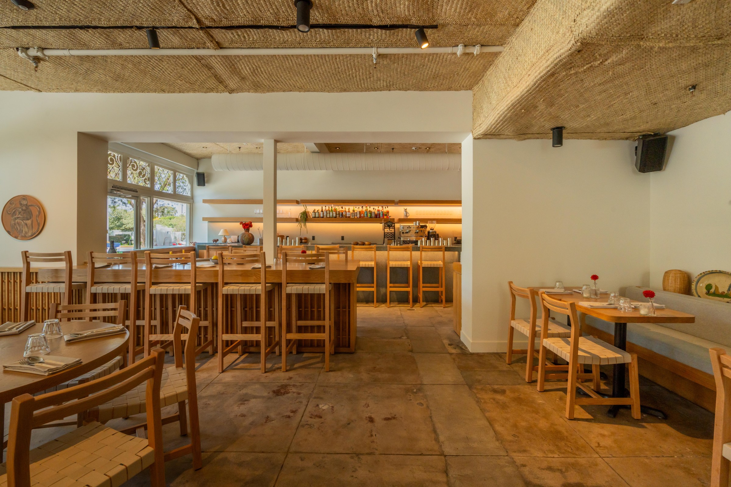 Dining room at San Damian in Venice with light woods, woven ceiling, and a downlit bar.