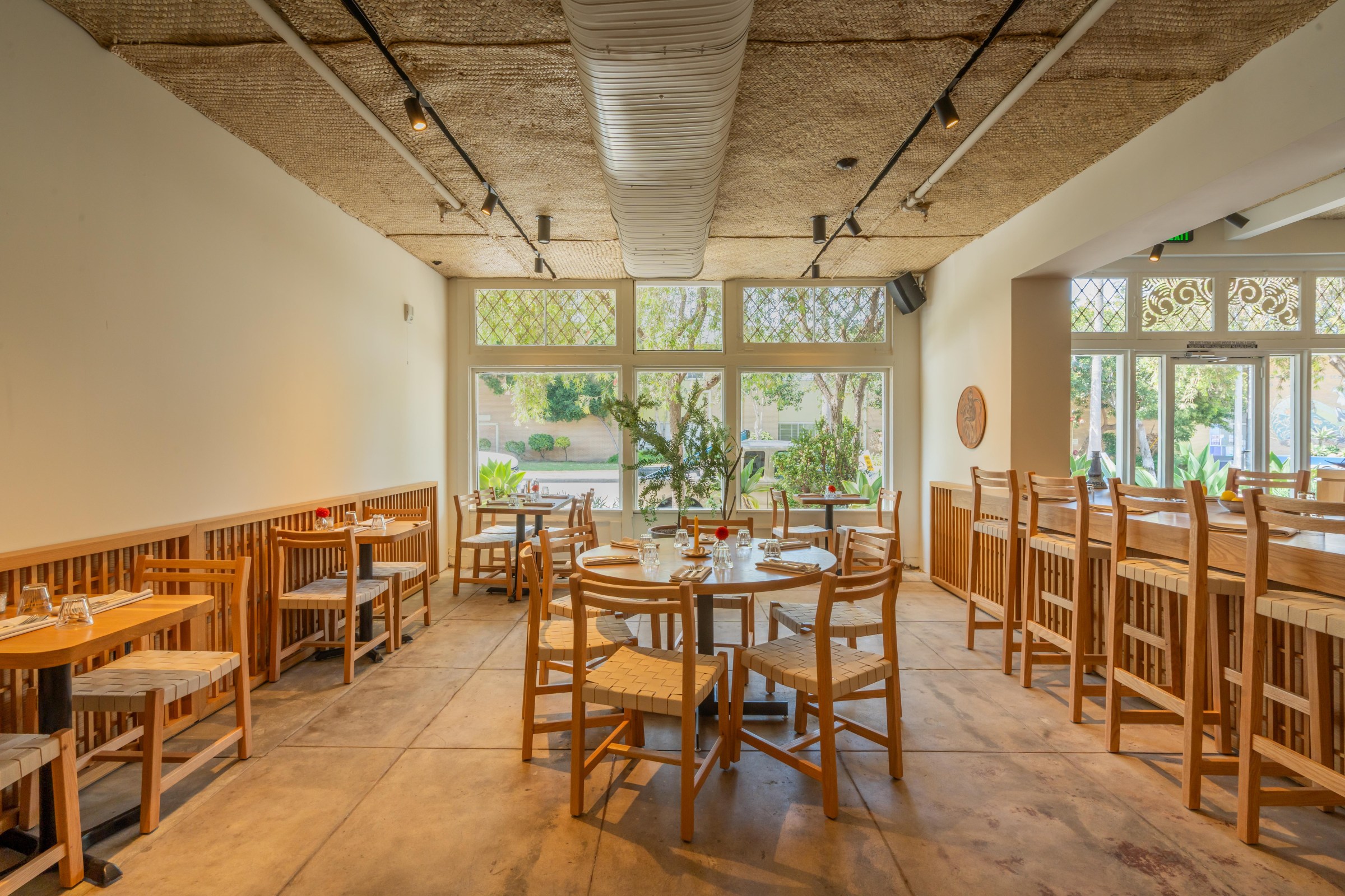 Interior of San Damian with a wall of windows and light wood tables.