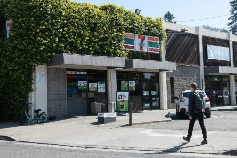 A person walks past an ivy-covered strip mall with a 7-Eleven