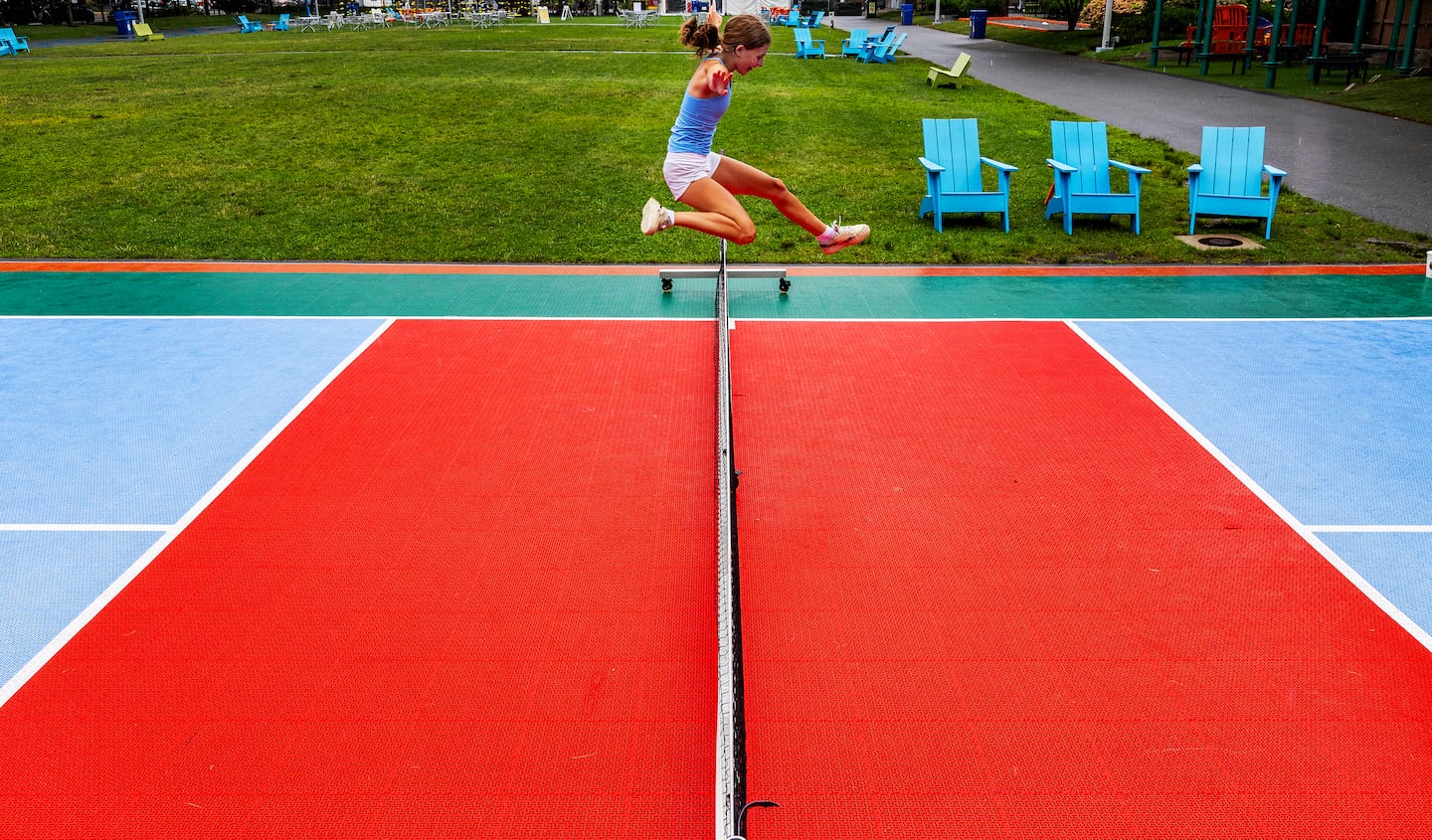 A teenager jumps over the pickleball net at Lawn on D.

